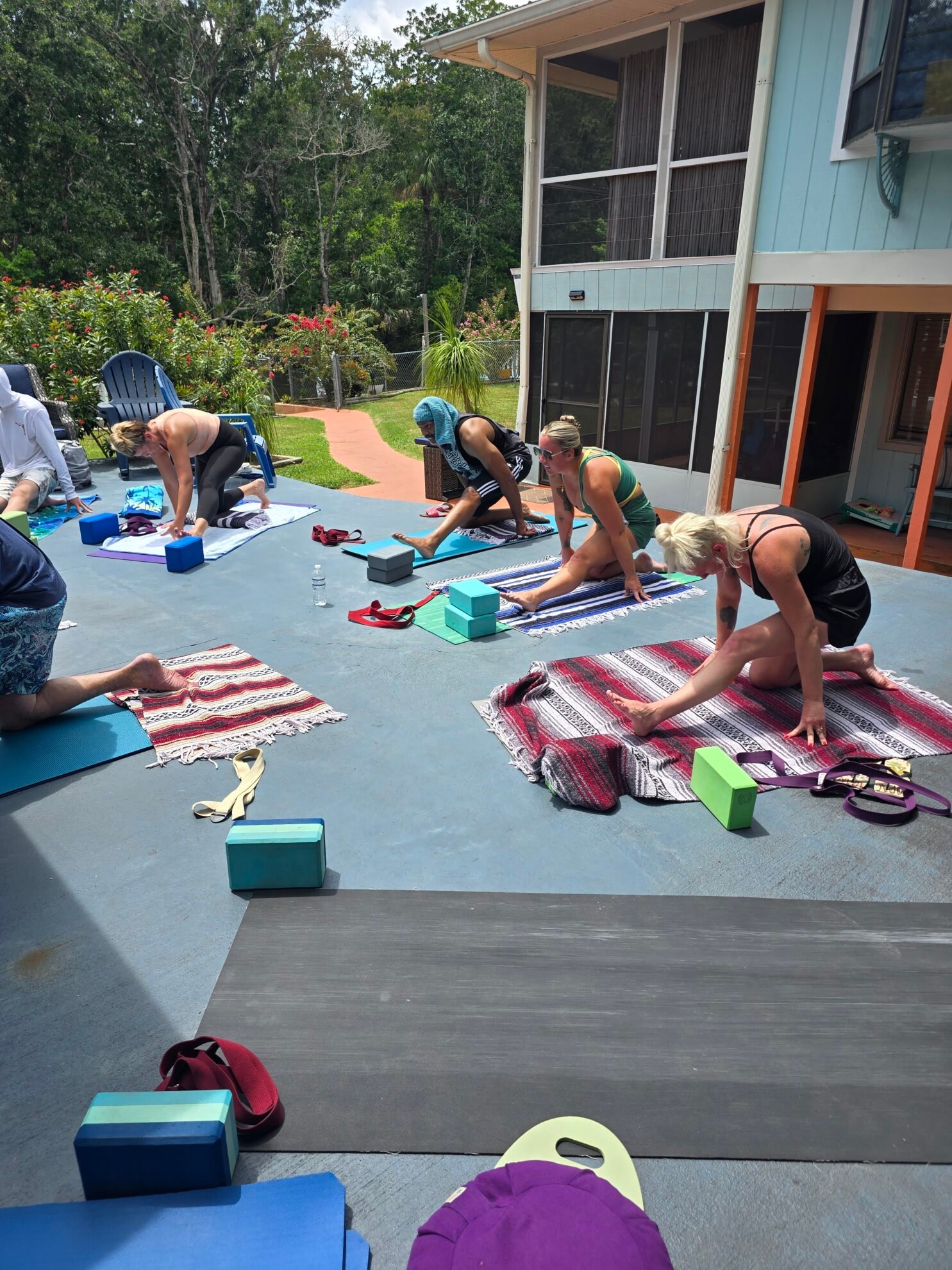 Yoga students in a half split hamstring stretch on mats and blankets during an outdoor Sacred Space Yoga class