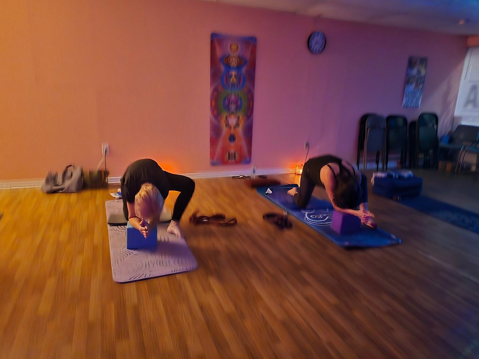 Two students kneeling with elbows on yoga blocks in a shoulder stretch during a Sacred Space Yoga class