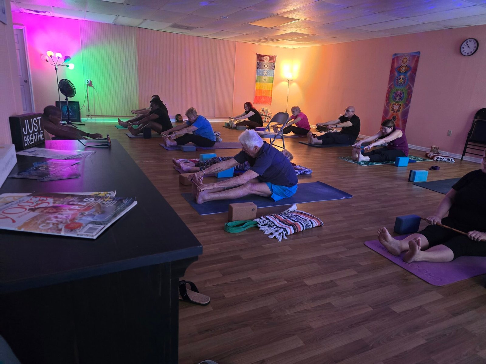 Students of all ages in a seated forward fold on yoga mats during a group class at Sacred Space Yoga