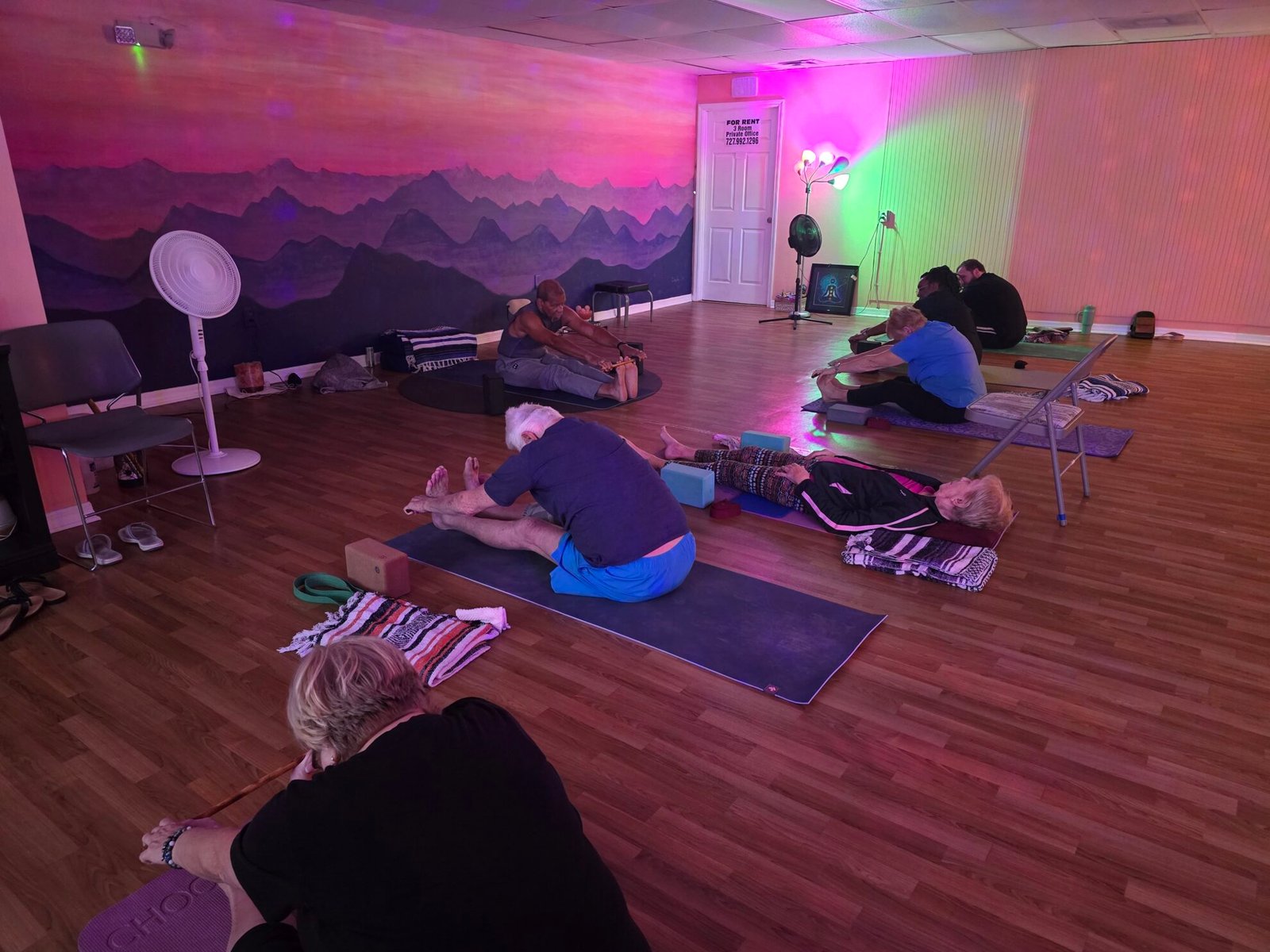 Students of all ages doing seated and reclined stretches on yoga mats during a class at Sacred Space Yoga