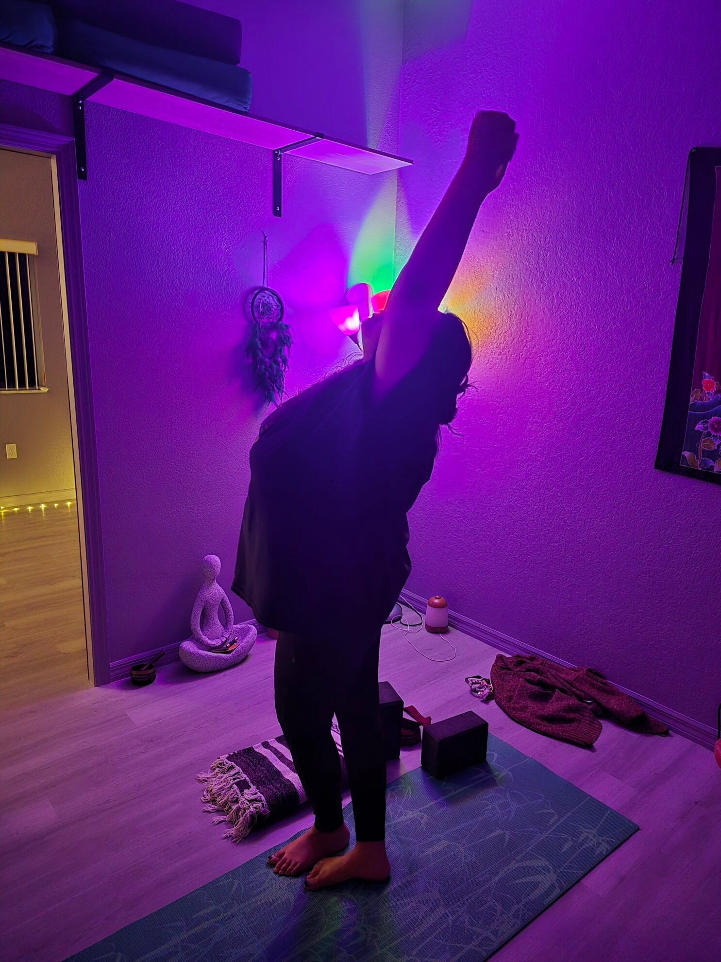 Woman in a standing side stretch with one arm reaching overhead in a purple-lit yoga room at Sacred Space Yoga