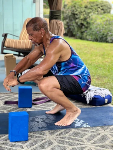 Instructor Darrell Whiteside of Sacred Space Yoga in a deep toe squat with arms reaching forward on an outdoor yoga mat